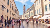 Gente caminando por una calle peatonal en una ciudad medieval llena de tiendas y un campanario