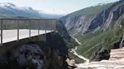 A viewing platform looking out to snowcapped mountains and a lush valley with a stream
