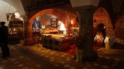 A medieval kitchen with a cloister vault ceiling, a fire and a large wooden dining table