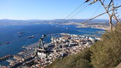 An aerial tram ascending a mountain above a coastal city