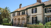 A 19th century manor house surrounded by rose bushes, shrubbery and palm trees