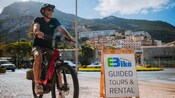 A man sitting on a bike next to a sign that reads E Bike Guided Tours and Rental