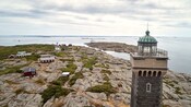 Uma costa rochosa com algumas casas e um farol com telhado em forma de cúpula.