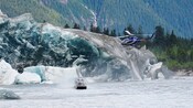 Un helicóptero sobrevuela la zona mientras una aerolancha revestida de vidrio navega las aguas glaciales