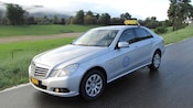A sedan with a sign on the roof that says TAXI is parked on a street next to grass and trees