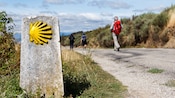 People with backpacks walking on a path past a stone mile marker