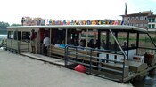 Passengers boarding an open air tourist boat docked on the edge of a river