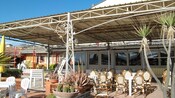 Una terraza para comer al aire libre que cuenta con mesas, sillas y macetas con plantas
