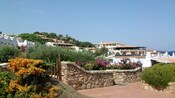 Buildings near a stone wall, a lush hillside and the ocean.