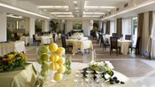 Área para sentarse en un restaurante, con mesas, sillas y jarrones llenos de manzanas, limones y limas
