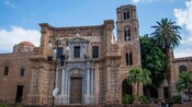 A stone church has a bell tower and three small domes