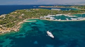 A yacht anchored near a slender penninsula with a lagoon and marina