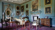 The interior of a room lined with old paintings, upholstered furniture and antiques