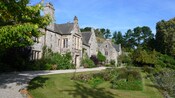 A stone manor house with a cobblestone driveway, lawn and garden