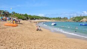 Kayaks and other watersports equipment on a sandy beach filled with people sunbathing and playing in the water