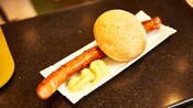 A grilled bratwurst with mustard and a bread roll
