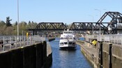 A triple deck tour boat filled with passengers sailing into a canal