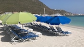 Outdoor recliners and umbrellas line the sand on a Caribbean beach, facing the water
