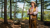 A member of a community indigenous to Goat Island stands in the forest with an intricately carved cane