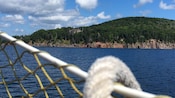 The view from a boat of a coastline with rocky cliffs, a thick forest and a big house