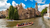 2 boats filled with passengers cruising through a historical waterway lined with centuries old brick buildings