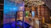 Wooden cylindrical rooms and a tall circular structure made of metal rods next to a staircase going down