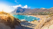 A view of the beach at Chania, Greece with people swimming and mountains in the background