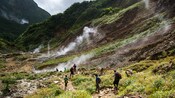 Hikers passing steaming rocks along a hillside trail