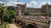 Guests walking over a stone bridge to a historic fortification with a door