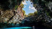 Guests in a small boat paddling the waters of an underground cave that looks out to the sky