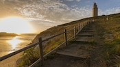 A stone lighthouse on a grassy hill next to the ocean