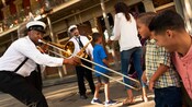A trombonist in a band uniform playfully interacts with young Guests