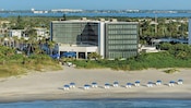 Lounge chairs and umbrellas situated on a sandy shoreline in front of the Hilton Cocoa Beach Oceanfront hotel
