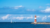 Sailboats sailing near a lighthouse on the water's edge