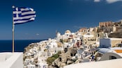 A Greek flag flying next to the water of an island with domed minimalist architecture
