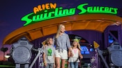 Una mujer y 2 niños parados frente a Alien Swirling Saucers