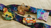 A Mickey Mouse print lanyard with 4 pins attached to it, each pin has the word play and an image. The first pin is Simba. The second pin is a yeti tearing up train tracks. The third pin is Lightning McQueen. And the fourth pin is Mike and Sulley opening a door.