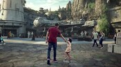 A little girl pulls her father towards the Millennium Falcon