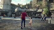A little girl pulls her father towards the Millennium Falcon