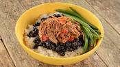 Uma tigela de ensopado de carne bovina, feijão-preto e vagem sobre arroz.