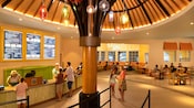 Une cafeteria avec une grande sculpture d’un parapluie, des lumières suspendues, un grand menu affiché sur le mur, des visiteurs qui commandent aux caisses avant et d’autres visiteurs assis qui mangent