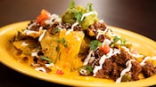 A plate of nachos topped with cheese sauce, ground meat, guacamole, cilantro and sour cream