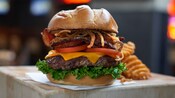 A burger piled high with lettuce, cheese, tomatoes, bacon and grilled onions