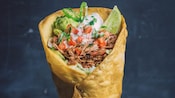 A beef mixture in a deep fried cone shaped tortilla shell garnished with onions, parsley and cilantro