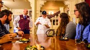A VIP Tour Guide watches as a chef presents a sample dish to Guests at a dining table