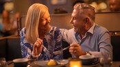 A man and woman smile at each other while sharing a dessert