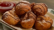 Five small pastry puffs drizzled with chocolate and powdered sugar