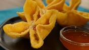 Three wontons on a plate next to a dipping sauce