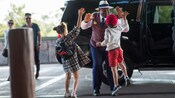 A VIP guide gives high fives to 2 young Guests outside a waiting luxury SUV