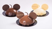 3 cakes shaped like Mickey Mouse with round chocolate ears. Text is written on the ears. One cake says Happy Birthday and another says Congratulations.